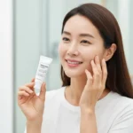 맑고 환해진 피부의 한국 여성이 함익병 미백연고로 알려진 기미 크림을 들고 자신감 있게 미소 짓는 모습, 2025년 피부과 미백 관리를 상징함.